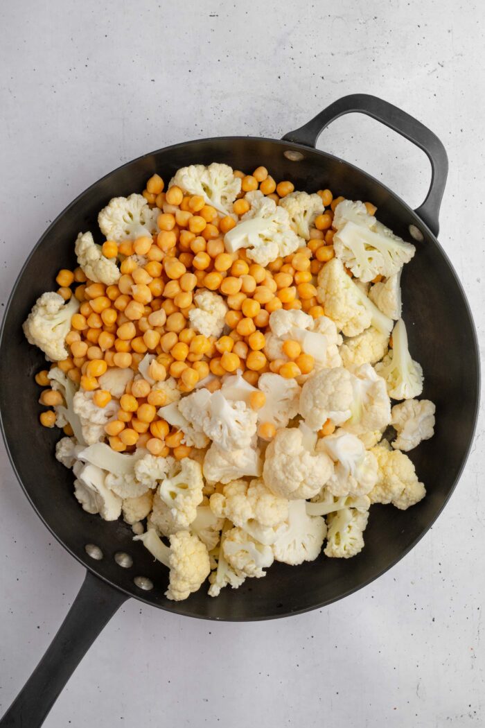 Chickpeas and cauliflower in a large cast iron skillet.