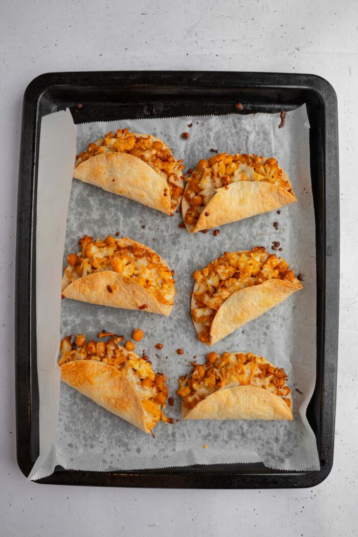Oven baked buffalo chickpea cauliflower tacos freshly out, still on a lined baking sheet.