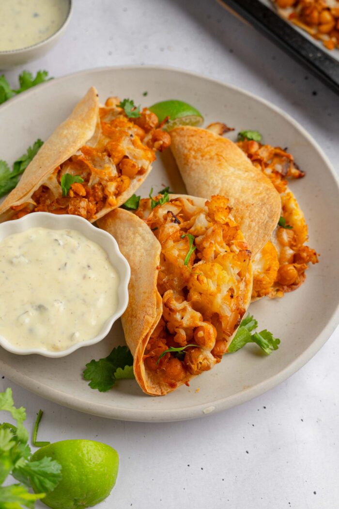 Three buffalo chickpea cauliflower tacos served on a plate with vegan caesar dressing on the side.