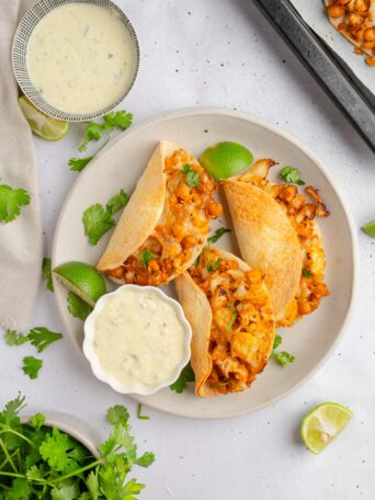 Top down view of three buffalo chickpea cauliflower tacos served on a plate with vegan caesar dressing on the side.