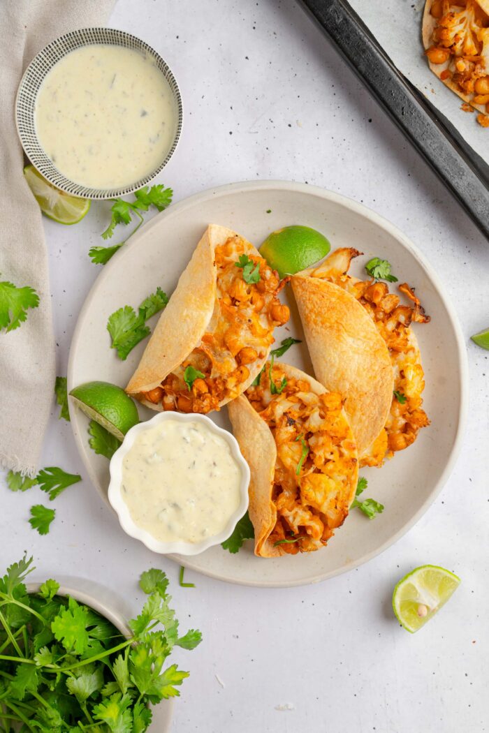 Top down view of three buffalo chickpea cauliflower tacos served on a plate with vegan caesar dressing on the side.