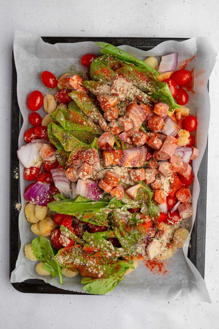 All of the ingredients, including veggies, gnocchi, and vegan sausage, added to a sheet pan and seasoned.