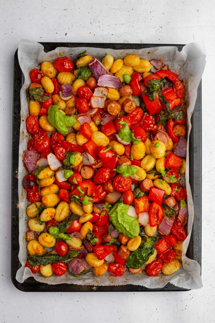 Generous helpings of vegan pesto added to the sheet pan of gnocchi with vegan sausage and pesto.