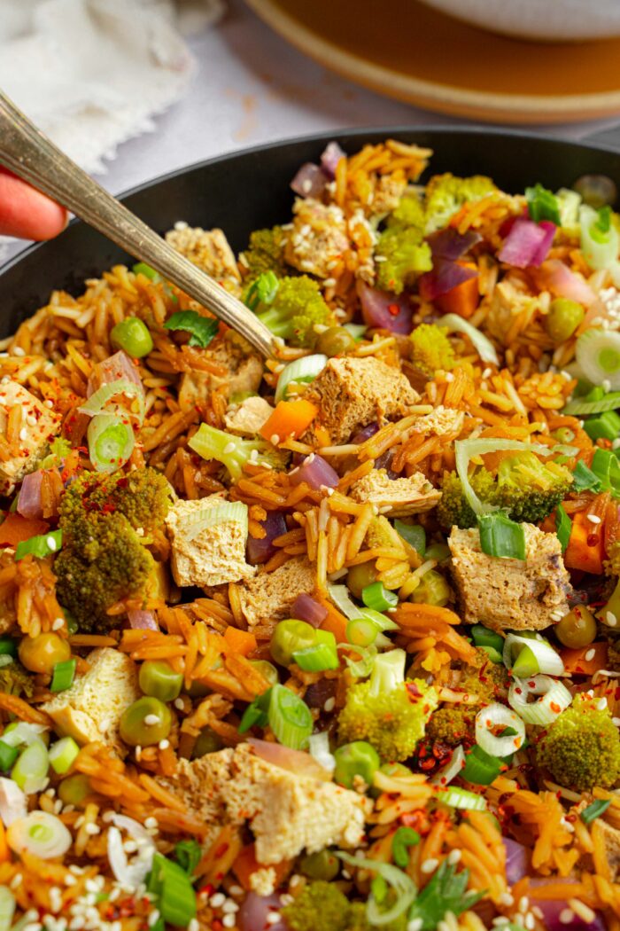 A close up of the pan with one pot veggie rice and a serving spoon sticking out.