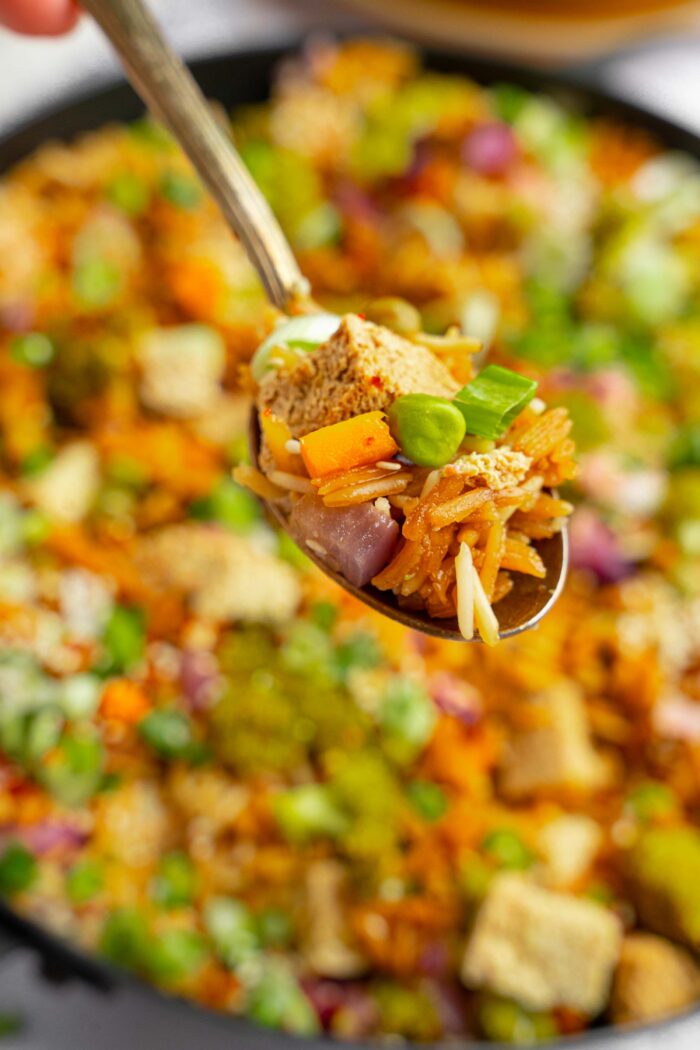 A close up of a spoonful of one pot veggie rice held up to the forefront of the shot.