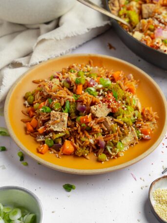 A plate of one pot veggie rice with spring onions and sesame seeds on top.