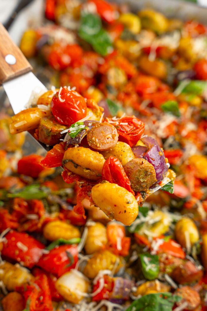 A close up of a serving spatula carryign some sheet pan gnocchi with sausage and pesto.