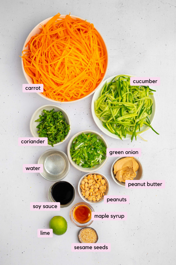 The ingredients to make carrot and cucumber salad laid out and labeled clearly on a white background.
