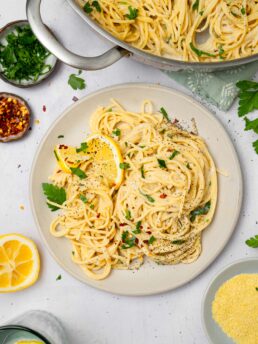 A top down view of easy vegan alfredo pasta served on a plate, with the rest of the dish visible in the photograph.