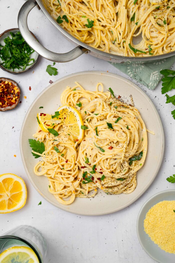 A top down view of easy vegan alfredo pasta served on a plate, with the rest of the dish visible in the photograph.