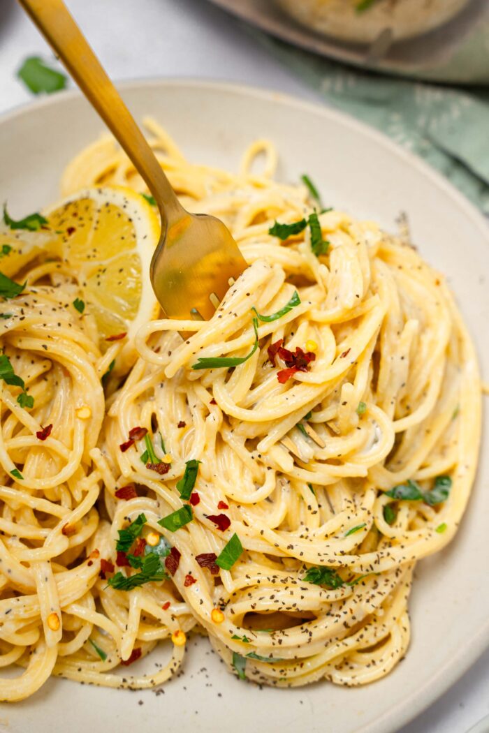 A close up of easy vegan alfredo pasta served on a plate and wrapped around a fork.