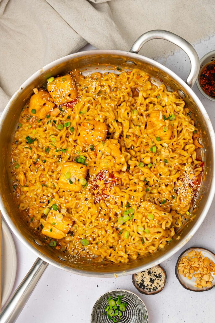 A large steel pan with the chili oil peanut noodles and scallions on top.