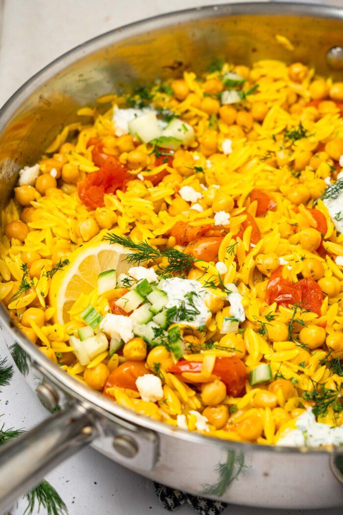 A pan with Mediterranean orzo bake, topped iwth vegan feta and fresh herbs.