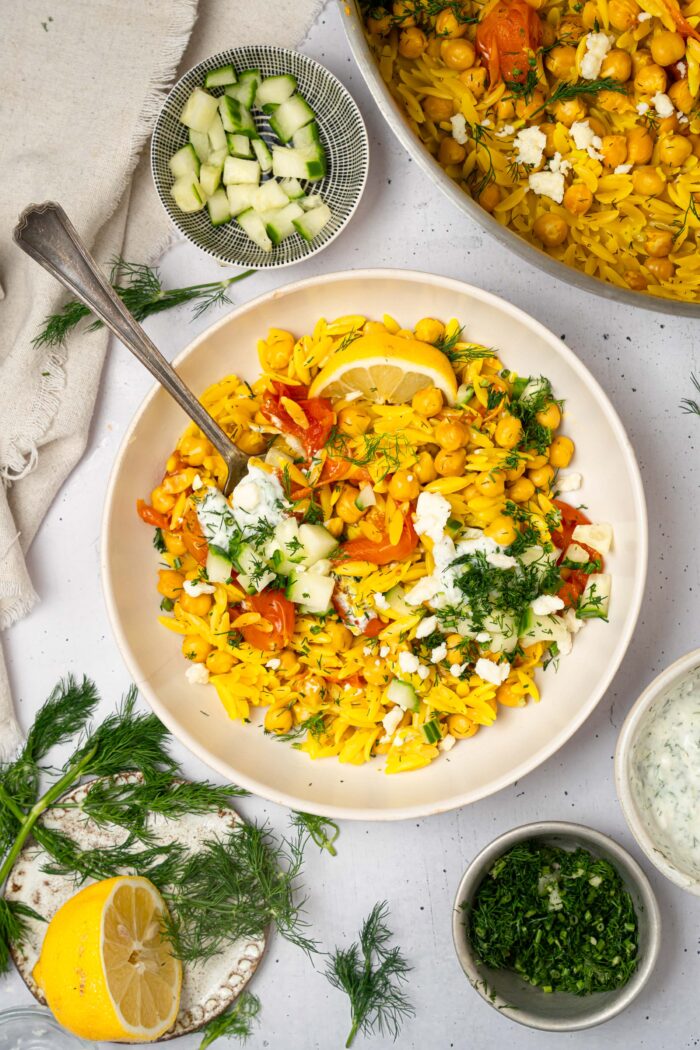 A serving of Mediterranean orzo bake in a bowl with vegan feta, lemon, and fresh herbs.