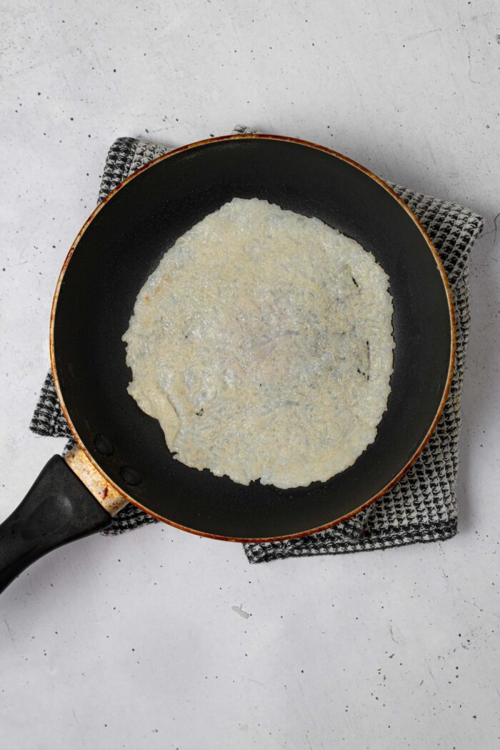 Rice tortilla being cooked in a frying pan.