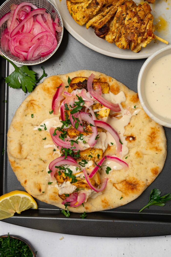 A warm vegan naan with "tofu skewer meat", tahini sauce, and red pickled onions.