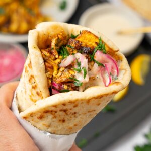 A hand holding up a serving of tofu skewers in a warm naan.