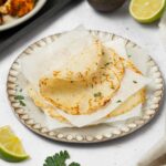Rice tortillas stacked and separated by parchment, with the top tortilla folded over.