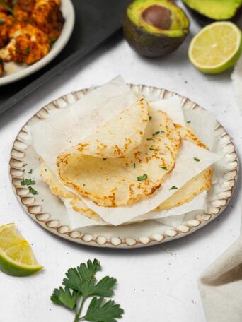 Rice tortillas stacked and separated by parchment, with the top tortilla folded over.