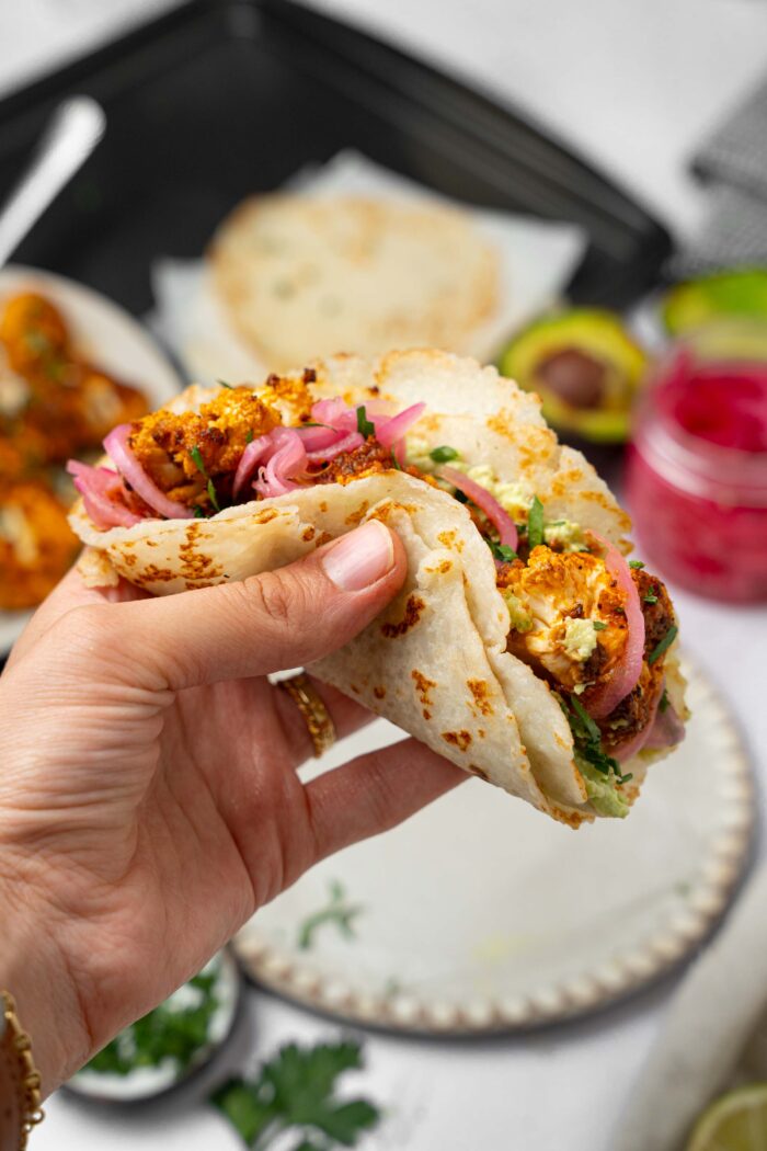 A hand holding up the cauliflower tacos made with rice tortillas.
