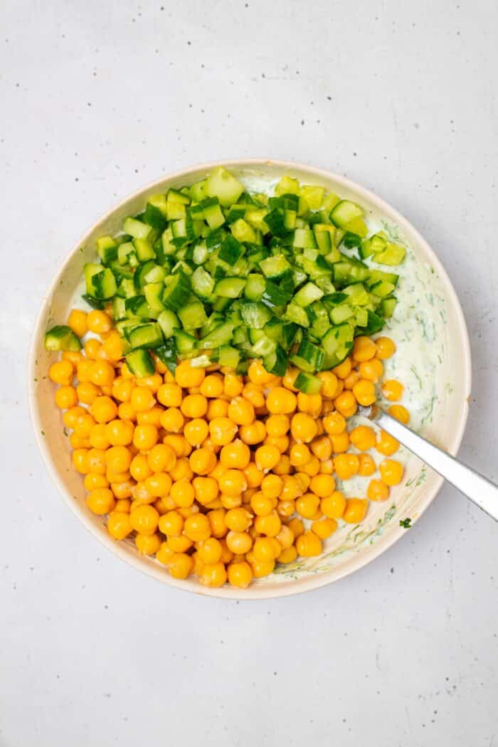 Chickpeas, cucumber, and dressing added to a shallow bowl.