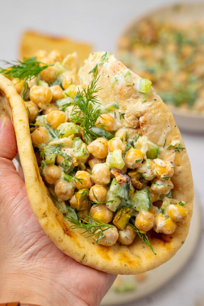 A hand holding a pita with a serving of tzatziki chickpea salad.