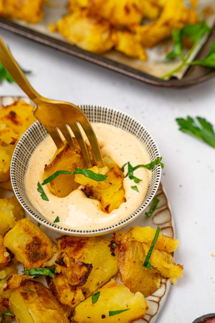 A fork picking up a piece of shaken potatoes and dipping it into sauce.