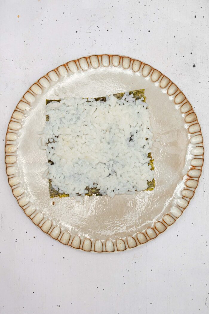 A small square of nori, with cooked sushi rice spread across the surface.