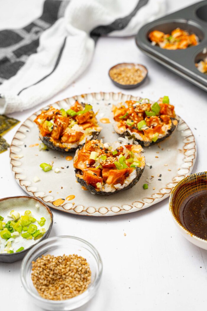Three sushi cups on a plate, served with spicy mayo, green onions and sesame seeds.