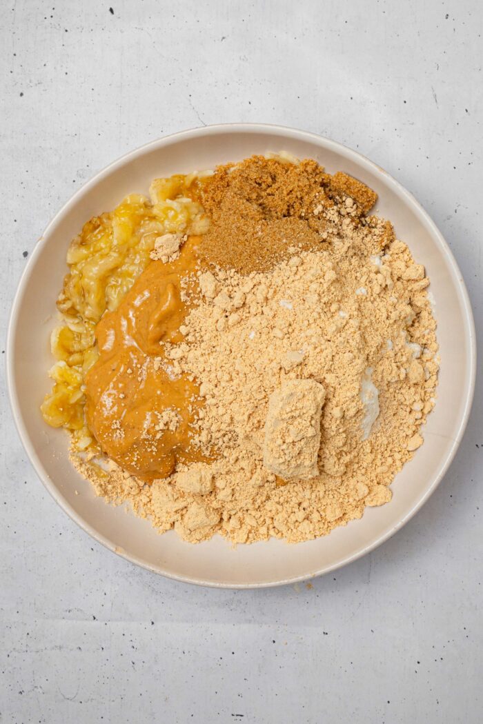 Dry ingredients and peanut butter added to the mashed bananas in the bowl.