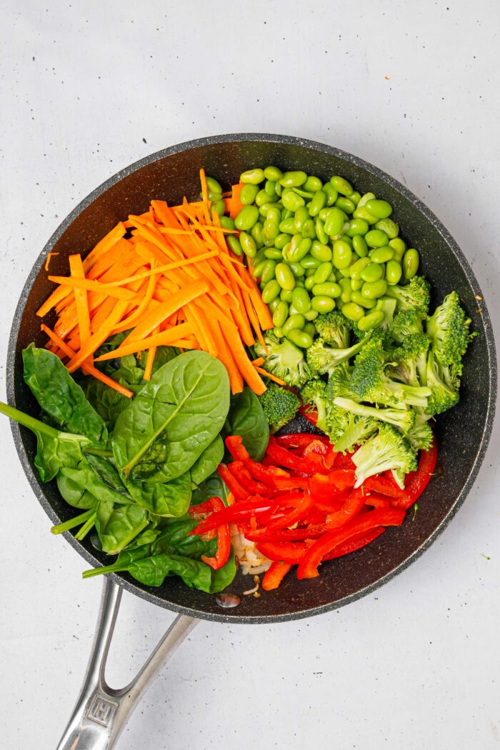 The veggies including carrot, spinach, bell pepper and edamame, laid out in a skillet.