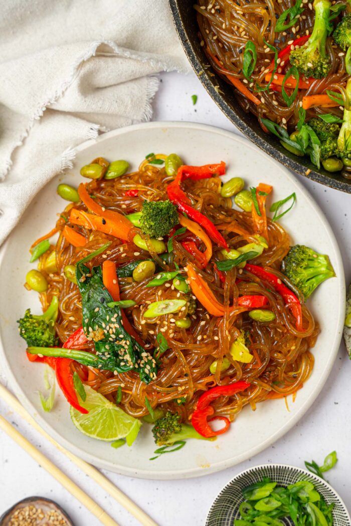 Glass noodle stir fry served on a plate topped with sesame seeds.