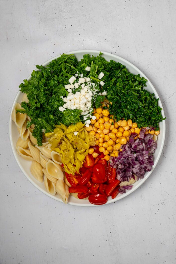 Vegetables, chickpeas, pasta shells, and vegan feta in a large salad bowl.