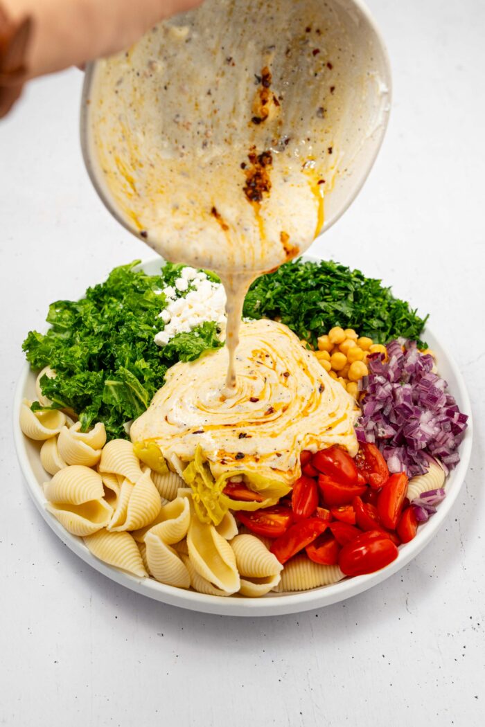 Spicy and creamy dressing being poured over the pasta and veggies for the spicy pasta salad.