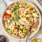 A bowl of spicy pasta salad with a spoon sticking out, and extra ingredients visible in the corners of the shot.