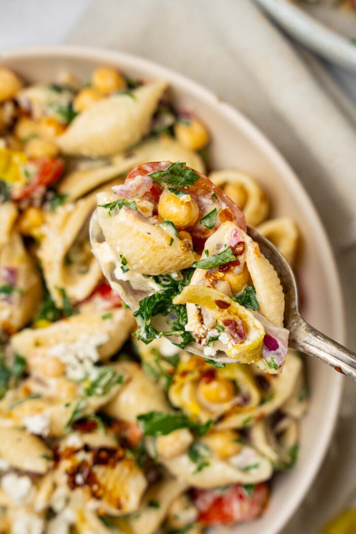 A close up of a spoonful of spicy pasta salad, with the rest of it visible in the background.