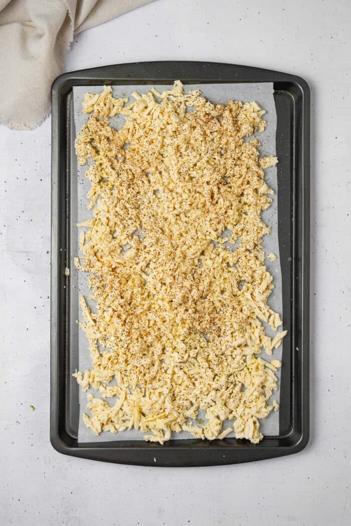 Grated tofu spread across a lined baking sheet in an even layer.
