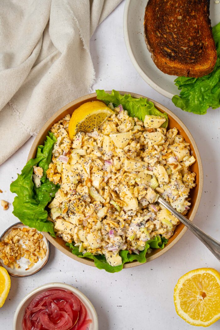 A bowl of shredded tofu salad with a serving spoon sticking out and some extra ingredients visible in the corners of the shot.