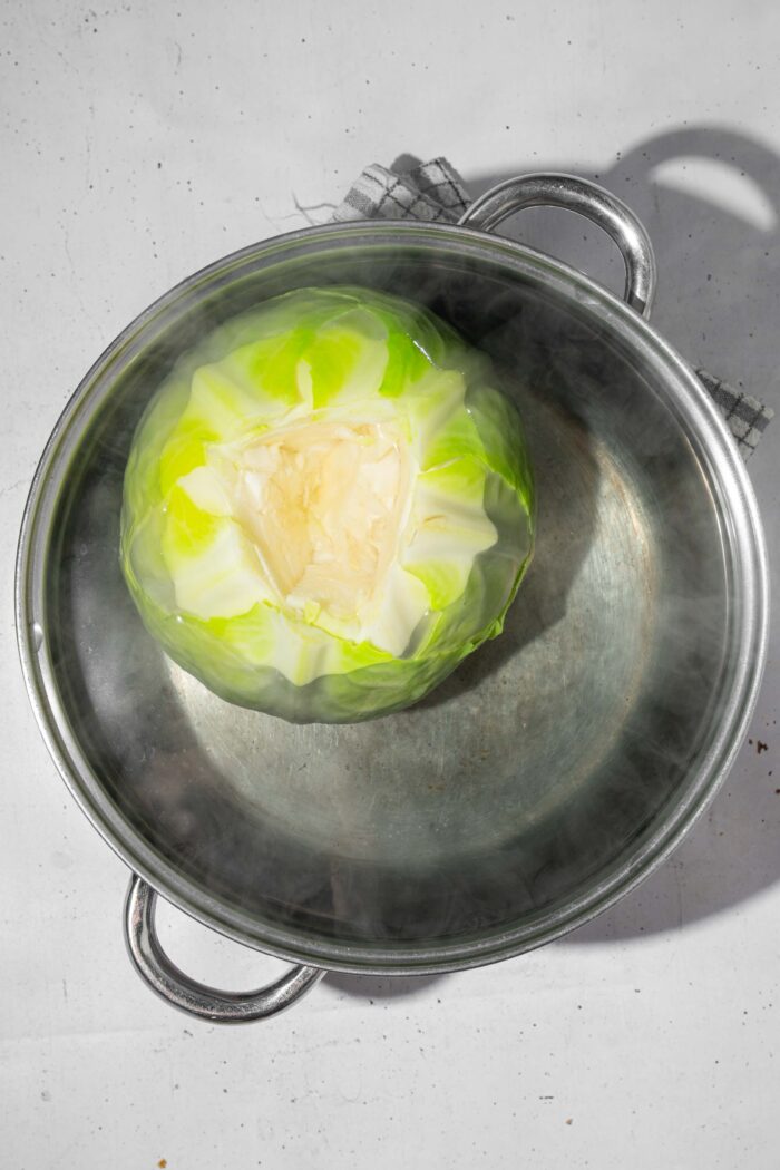 A head of cabbage fully submerged in a pot of boiling water.