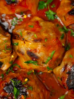 A close up of one vegan cabbage roll, surrounded by others and covered in sauce.