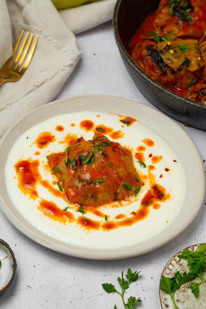 One of the vegan cabbage rolls served on a plate with extra sauce drizzled around.