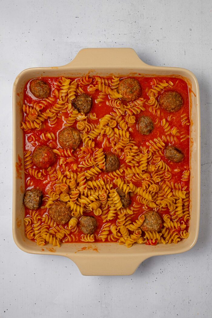 The pasta, sauce, and vegan meatballs mixed together in a casserole dish.