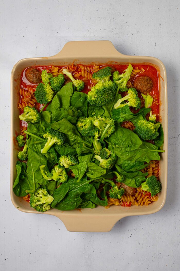 Broccoli and spinach added on top of the pasta and meatball mixture in the casserole dish.