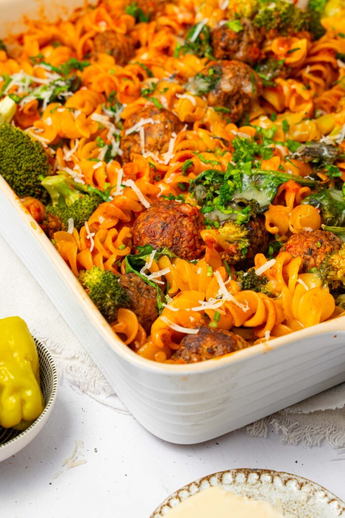 A casserole pan with vegan pasta and meatball bake, served with plant-based cheese and fresh herbs.