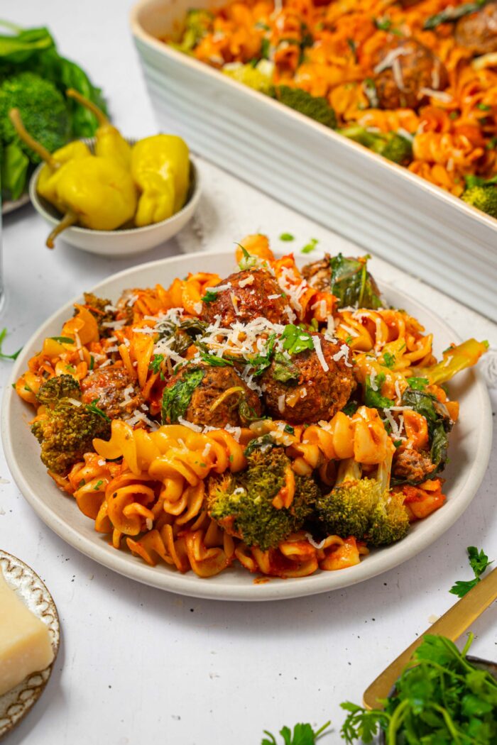 A serving of vegan pasta and meatball bake on a plate, with vegan cheese as a topping.
