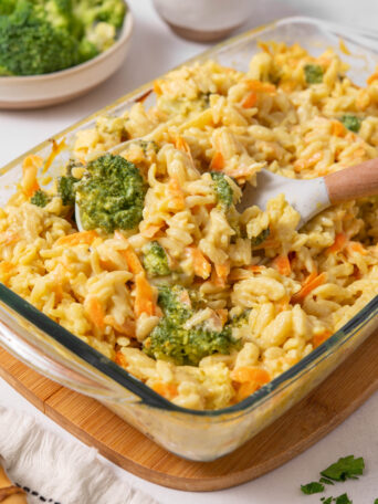 A close up of the casserole dish with vegan broccoli cheddar orzo, and a wooden serving spoon sticking out of it.