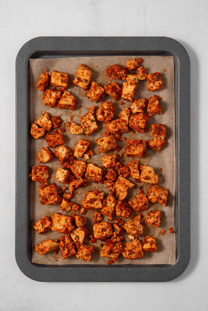 Tofu cubes coated in spices and laid out on a lined baking sheet.