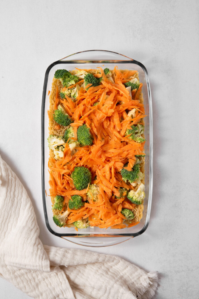 The veggies laid out on top of the pasta in a casserole dish to make vegan broccoli cheddar orzo.