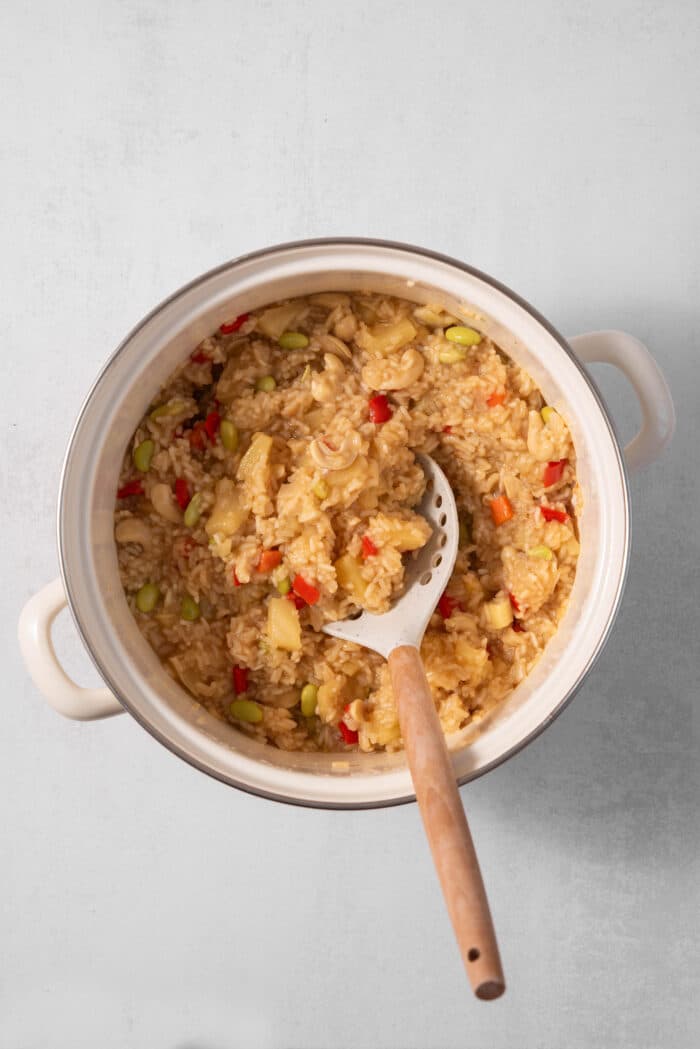 The pineapple rice mixed together with a wooden serving spoon in the pan.