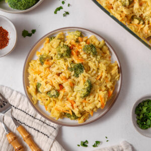 A serving of vegan broccoli cheddar orzo on a plate, with other ingredients visible in the frame.